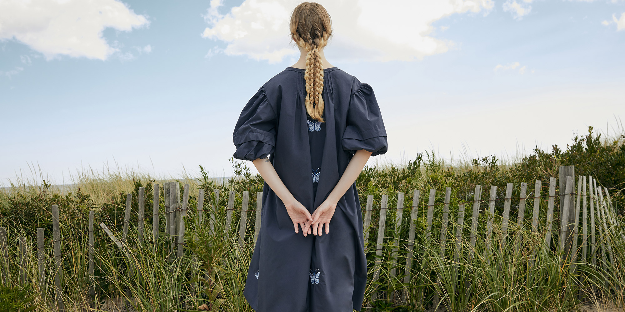 Nish Niche butterfly-embroidered dress against coastal dunes